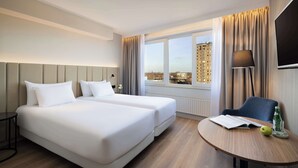 Habitación de hotel con dos camas, una mesa redonda con un libro y una manzana, una silla y un televisor en la pared.