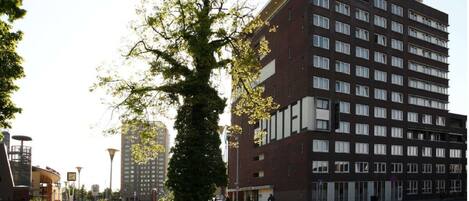 A multi-story hotel with a modern design, featuring a prominent entrance and a large tree in front.