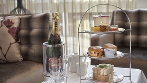 A three-tiered dessert stand with various pastries and a bottle of champagne on a table. - Doubletree by Hilton Hotel Woking (Woking)