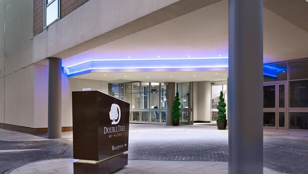 A hotel entrance with a reception desk labeled "DOUBLETREE BY HILTON" and a sign pointing to the reception. - Doubletree by Hilton Hotel Woking (Woking)