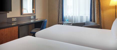 A hotel room with a bed, a desk, a chair, a TV, and a lamp.