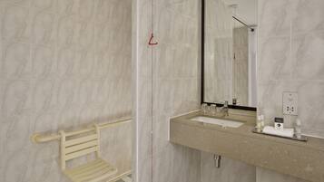 Un baño moderno con ducha, inodoro con barra de apoyo, lavabo con espejo y artículos de aseo en la encimera.