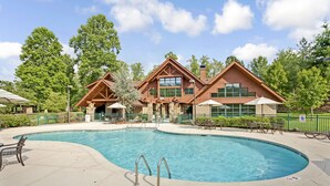 A pool area with a wooden building, lounge chairs, and umbrellas.