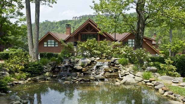A lodge with a pond, surrounded by trees and a mountain view.