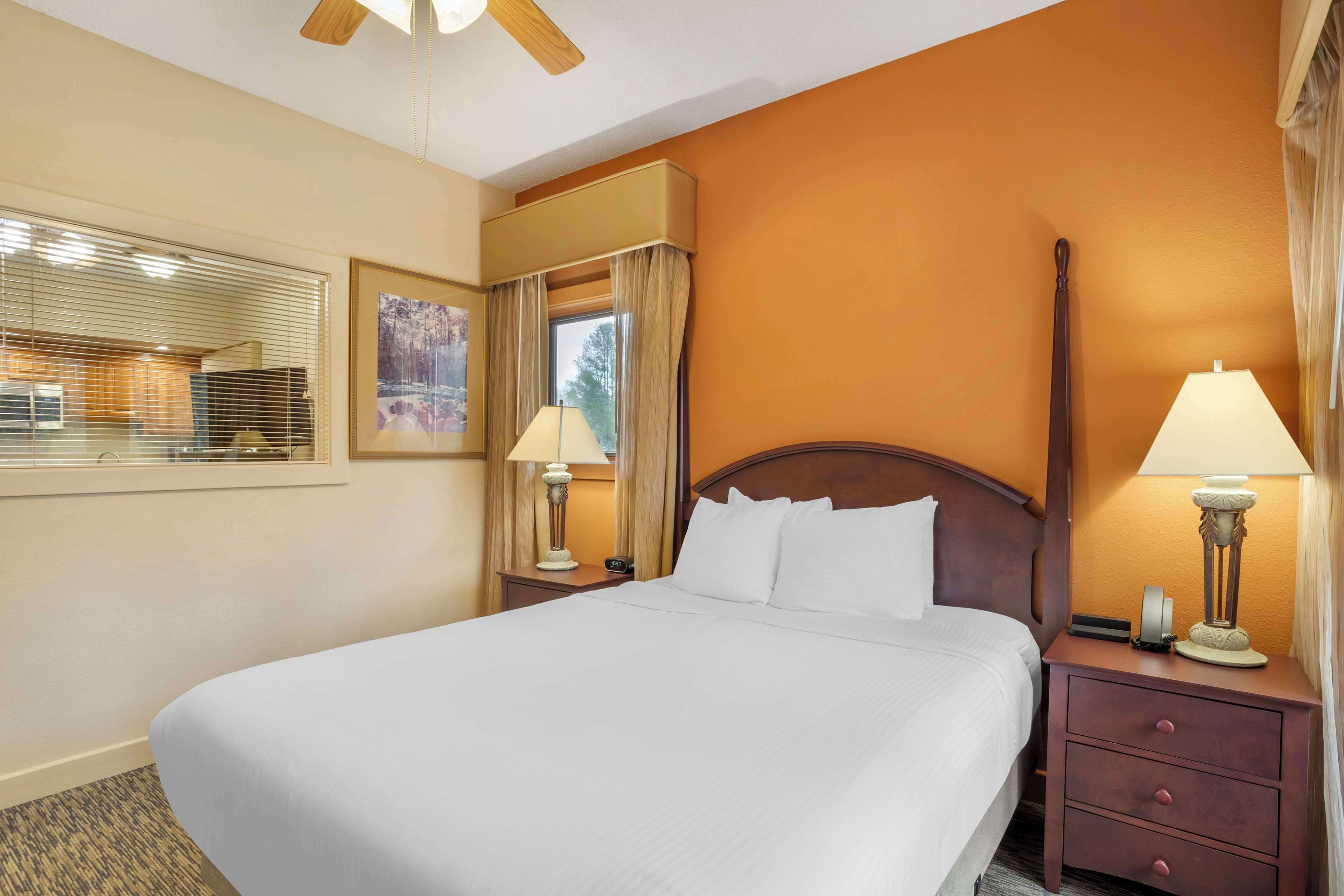 Una habitación de hotel con una cama grande, dos mesitas de noche con lámparas, una ventana con persianas y un cuadro en la pared.