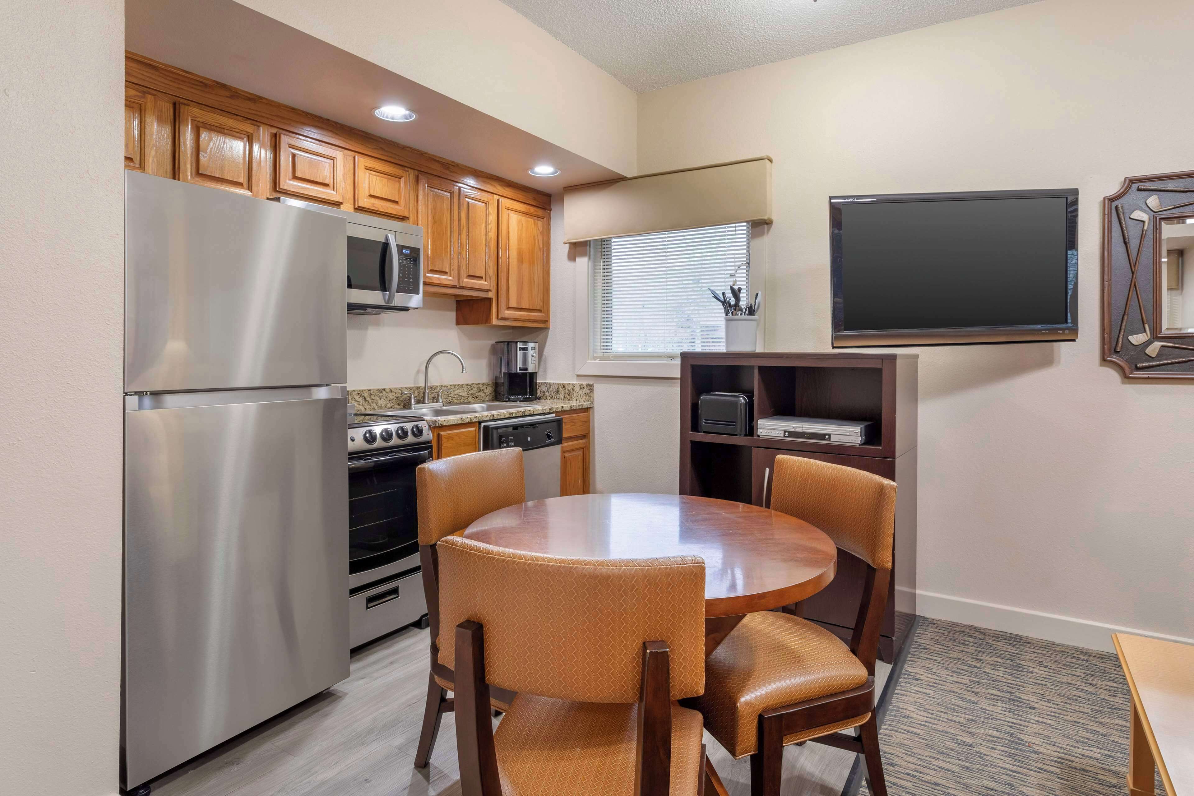 Una cocina compacta con electrodomésticos modernos, un comedor con cuatro sillas y un televisor de pantalla plana montado en la pared.
