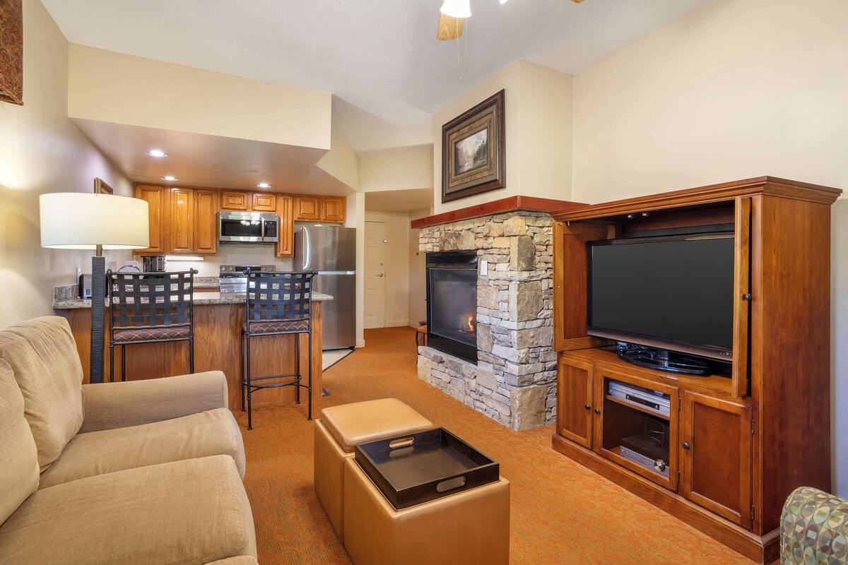 A modern living room with a fireplace, a television, and a kitchen area with wooden cabinets and appliances.