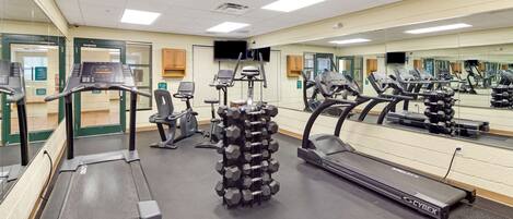 A gym with treadmills, elliptical machines, and a mirrored wall.