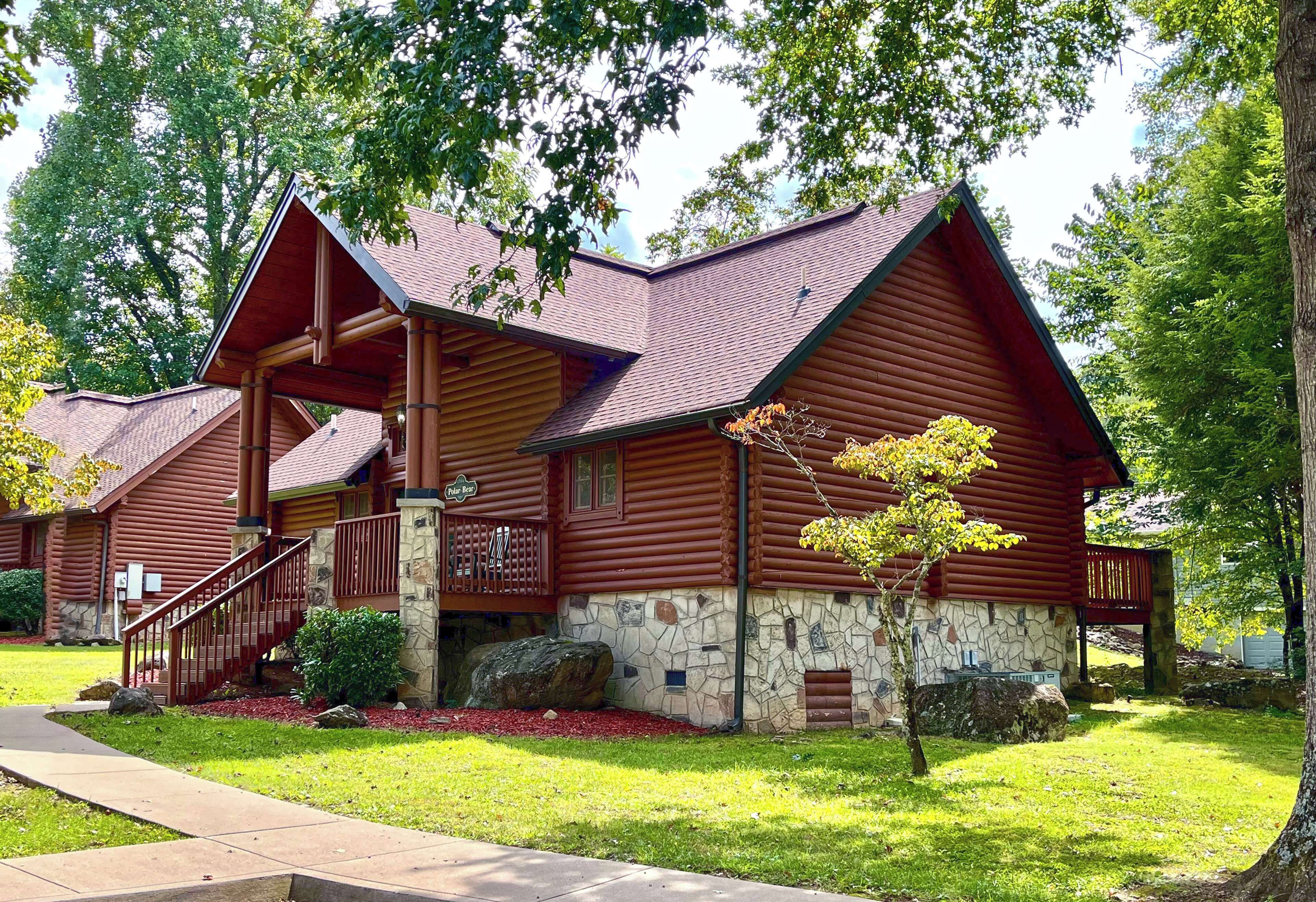 A log cabin-style building with a stone foundation, a wooden deck, and a staircase leading to the entrance.