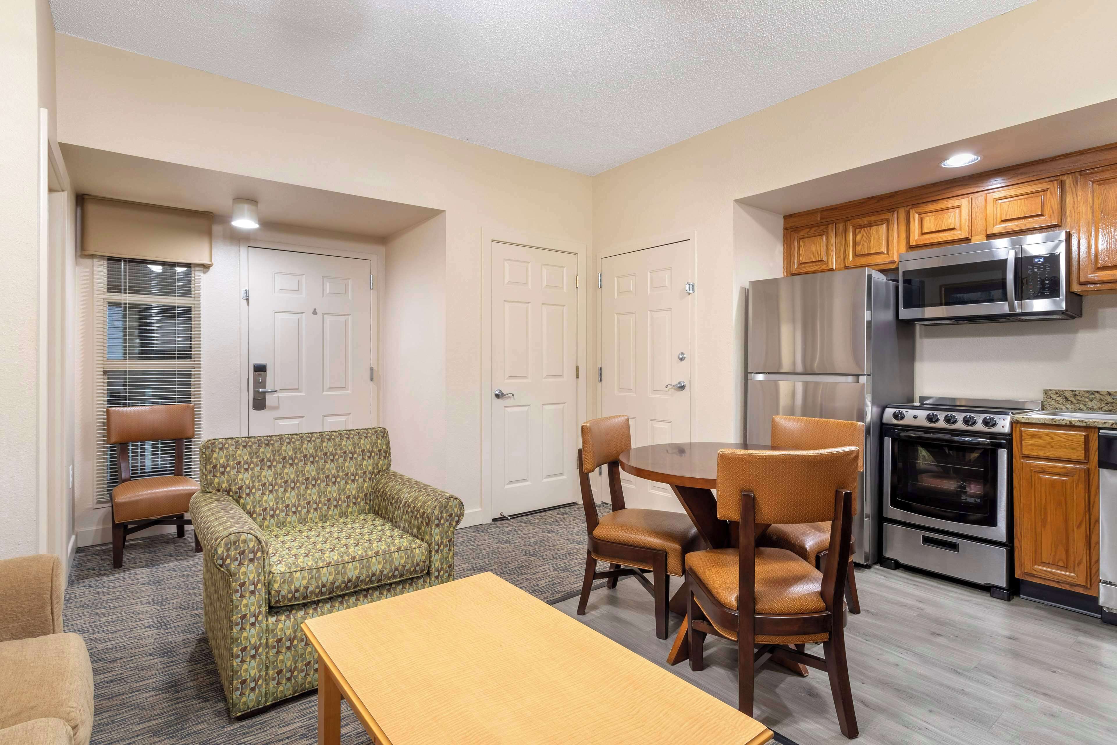A compact kitchen with modern appliances, a dining area with a table and chairs, and a patterned sofa.