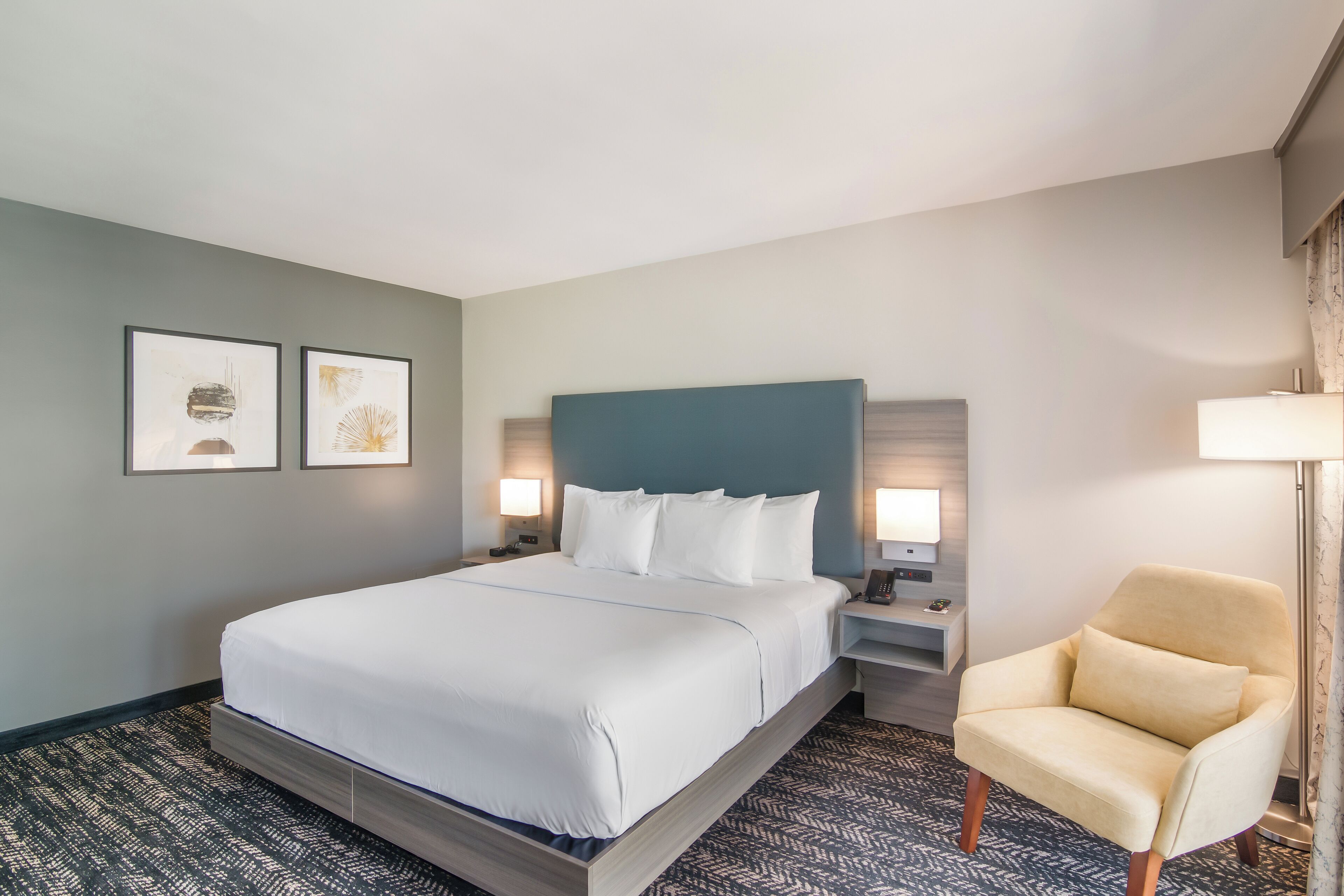 A hotel room with a large bed, two bedside tables with lamps, a chair, and two framed pictures on the wall.