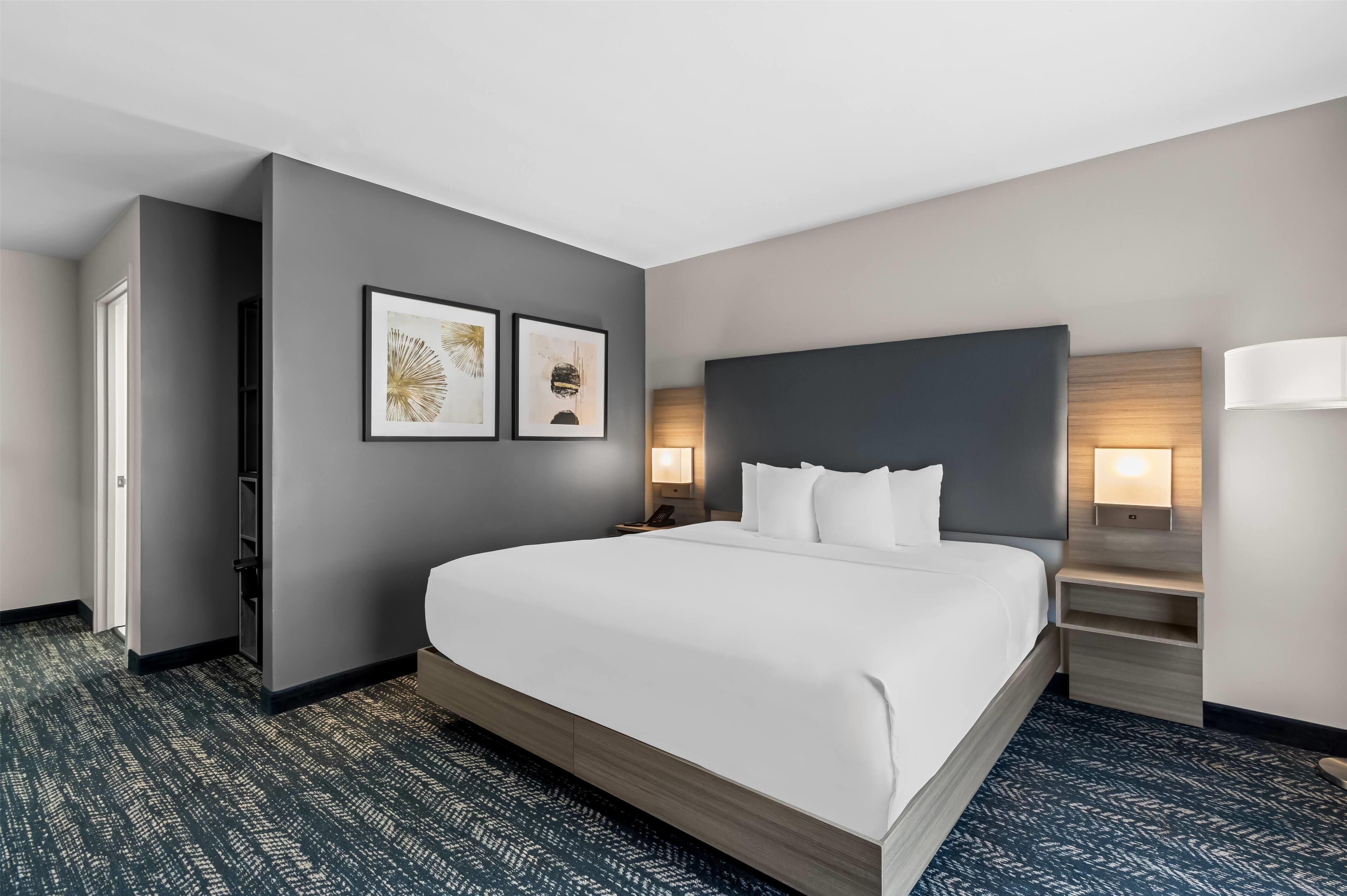 Een hotelkamer met een groot bed, een nachtkastje met een lamp en twee foto's in lijsten aan de muur.