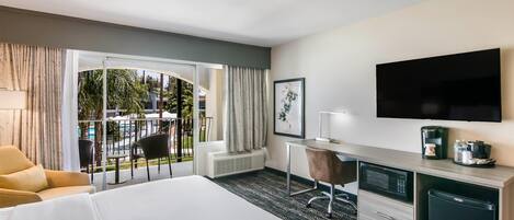 Habitación de hotel con cama, escritorio con silla, televisión, refrigerador pequeño y vista al exterior.