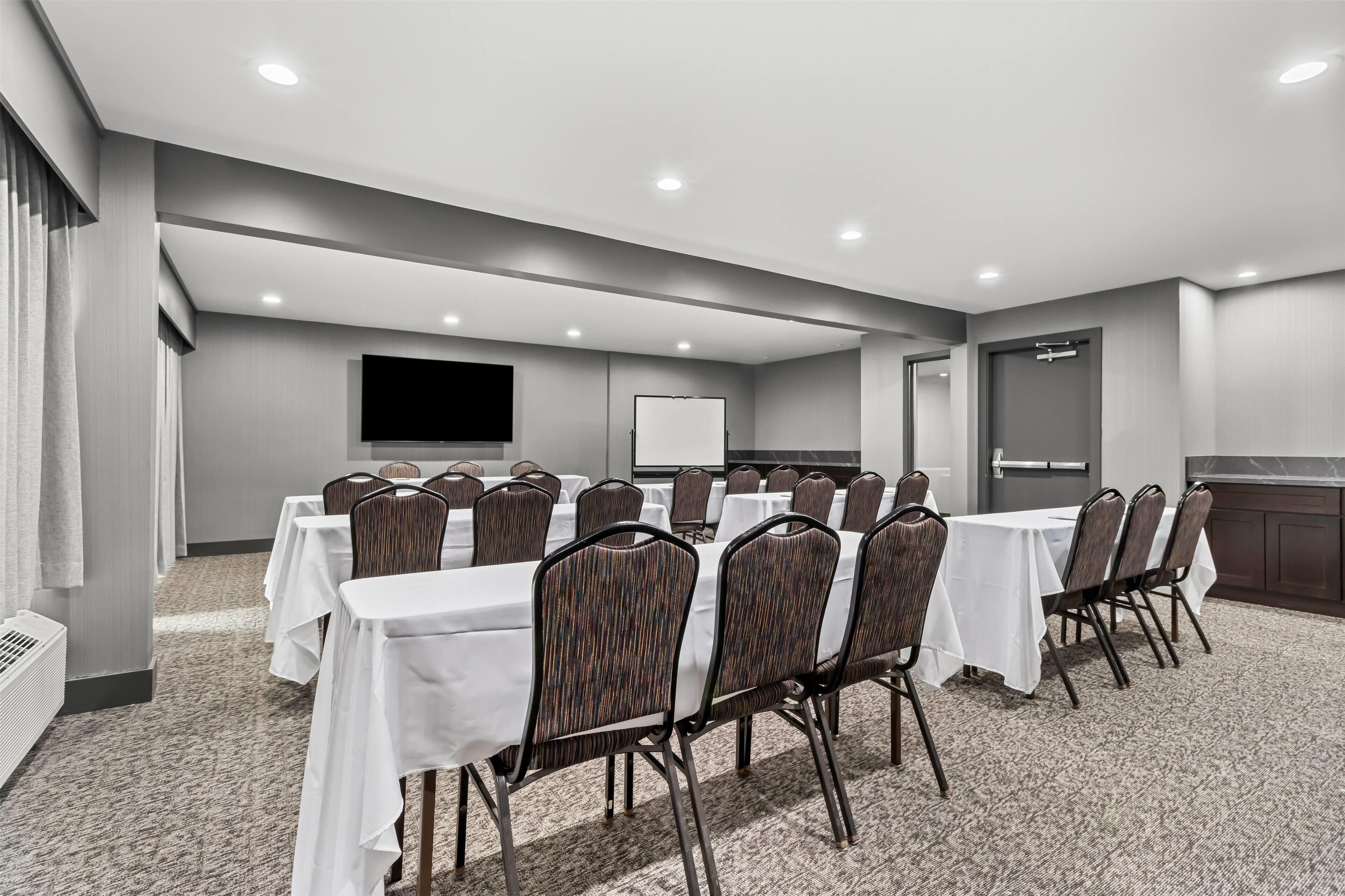 A conference room with tables and chairs, a flat-screen TV, and a whiteboard.
