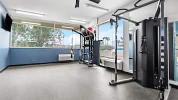 A gym with exercise equipment, large windows, and a ceiling fan.