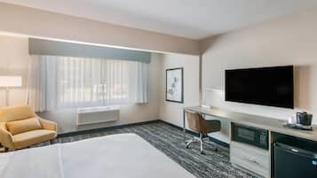 A hotel room with a bed, a desk, a chair, a flat-screen TV, and a minibar.