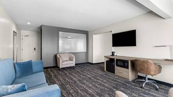 A hotel room with a blue sofa, a desk with a computer, a chair, a TV, and a large window.
