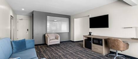 Habitación de hotel con sofá azul, escritorio con computadora, silla, televisor y ventana grande.