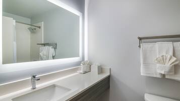 A modern bathroom with a large mirror, a white sink, a towel rack, and a toilet.