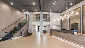 A spacious lobby with a staircase, a reception desk, and a modern chandelier.