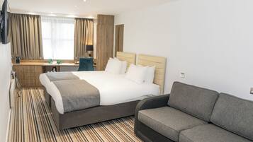 A hotel room with a large bed, a sofa, a desk, and a TV mounted on the wall.