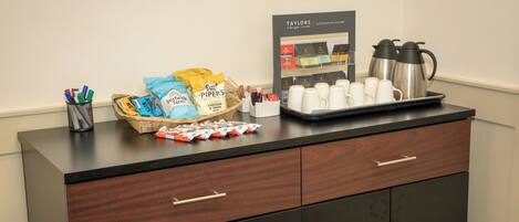 A counter with tea bags, coffee pots, and snacks.