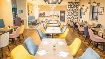 A restaurant with multiple dining tables and chairs, a bar area, and a patterned wall.