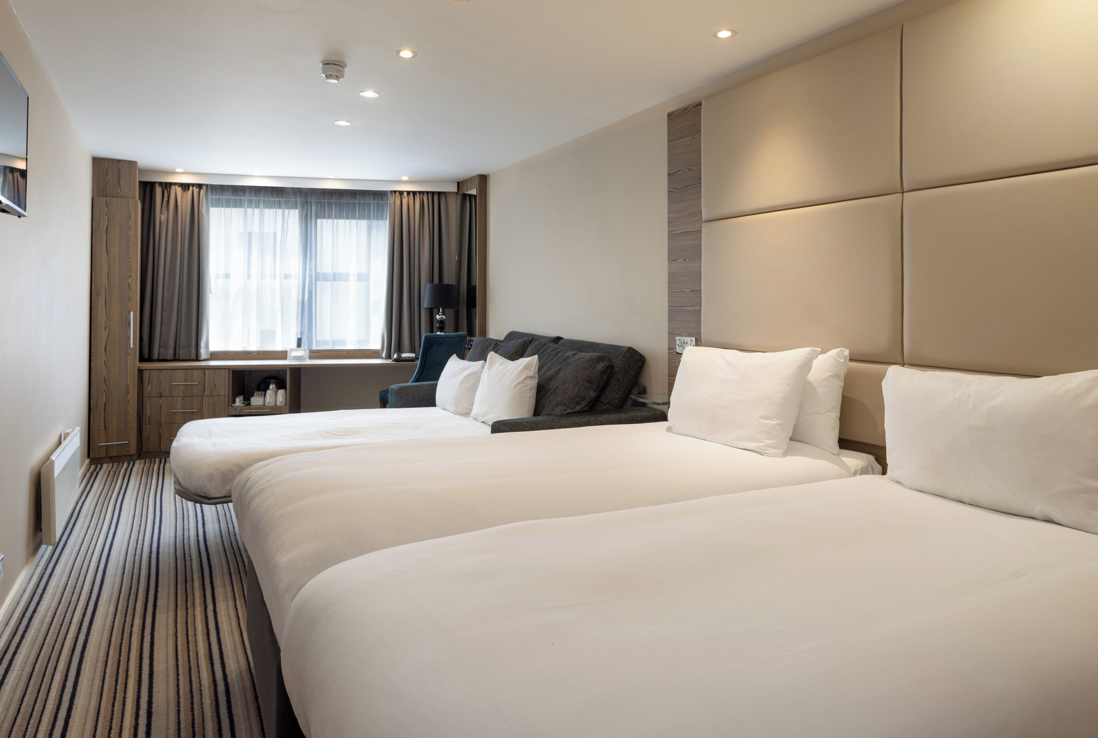A hotel room with two beds, a desk, a chair, and a large window with curtains.