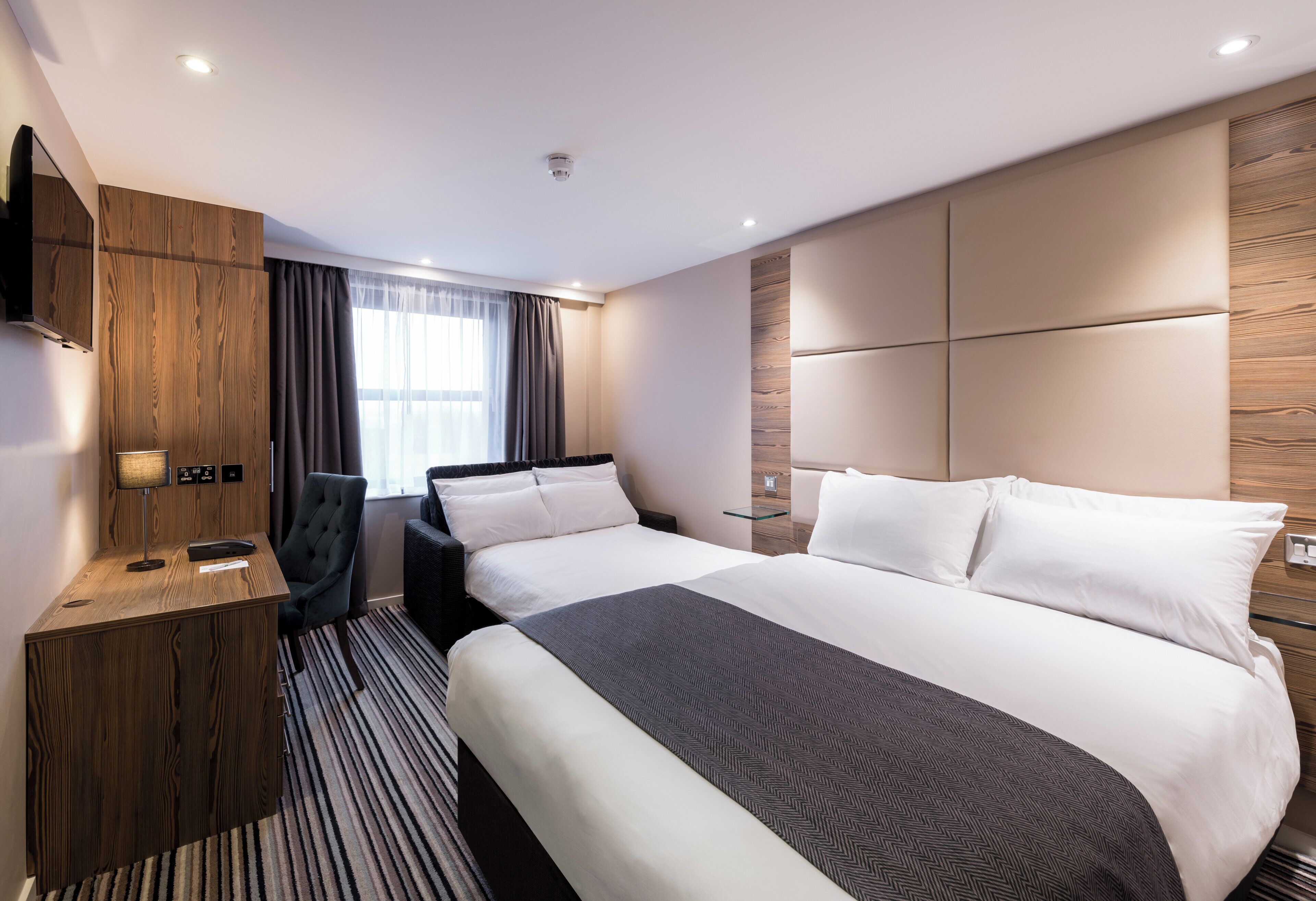 A hotel room with a large bed, a desk, a chair, and a television.