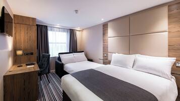 A hotel room with a large bed, a desk, a chair, and a television.