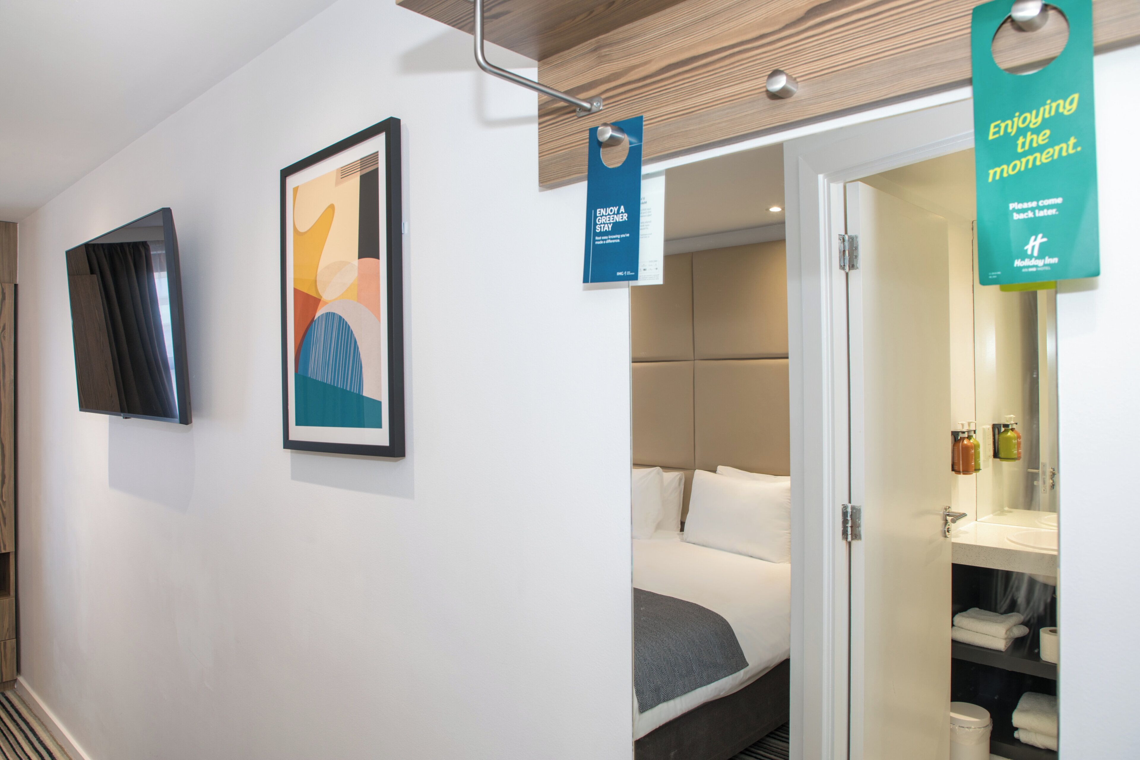 Une chambre d’hôtel comprenant un lit, une salle de bain et un couloir agrémenté d’œuvres d’art et de panneaux indicateurs.