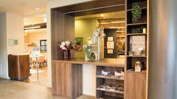 Un mostrador de recepción con detalles de madera, una vitrina con revistas y una pequeña planta a la derecha.