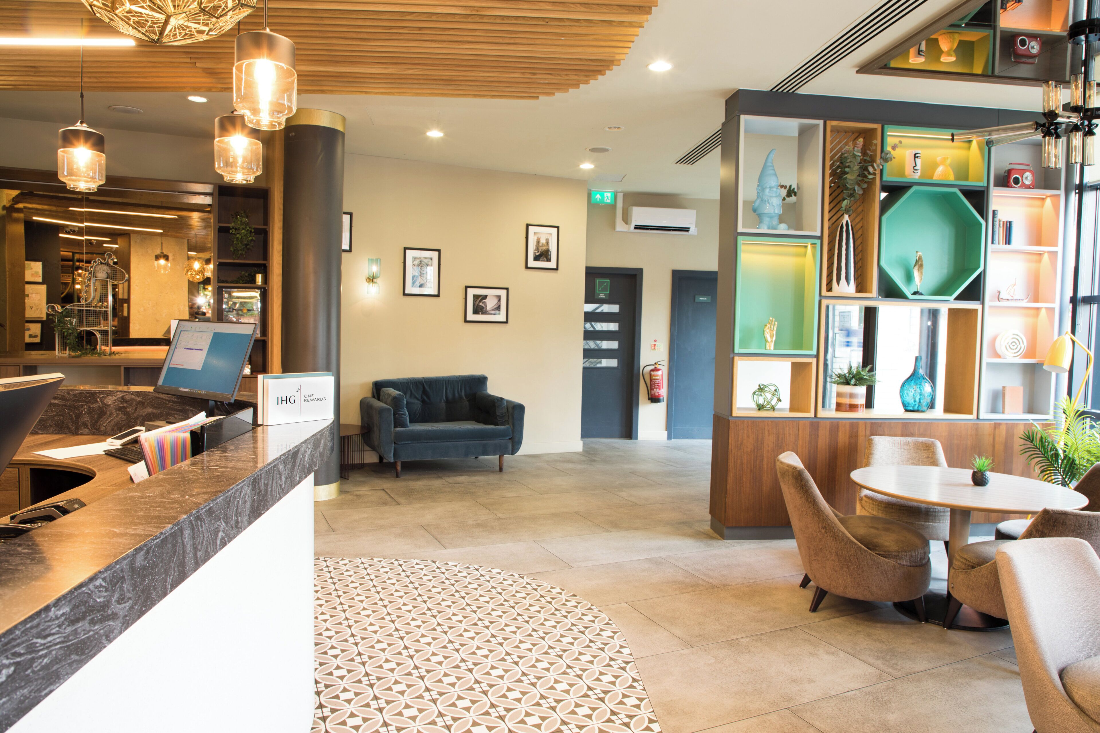 A reception area with a reception desk, a blue sofa, a small table with chairs, and a decorative wall with various items.