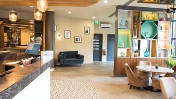 A reception area with a reception desk, a blue sofa, a small table with chairs, and a decorative wall with various items.