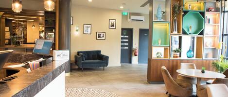 A reception area with a reception desk, a blue sofa, a small table with chairs, and a decorative wall with various items.