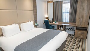 A hotel room with a large bed, a desk, a chair, a mirror, and a wardrobe. - Holiday Inn York City Centre by IHG (York)