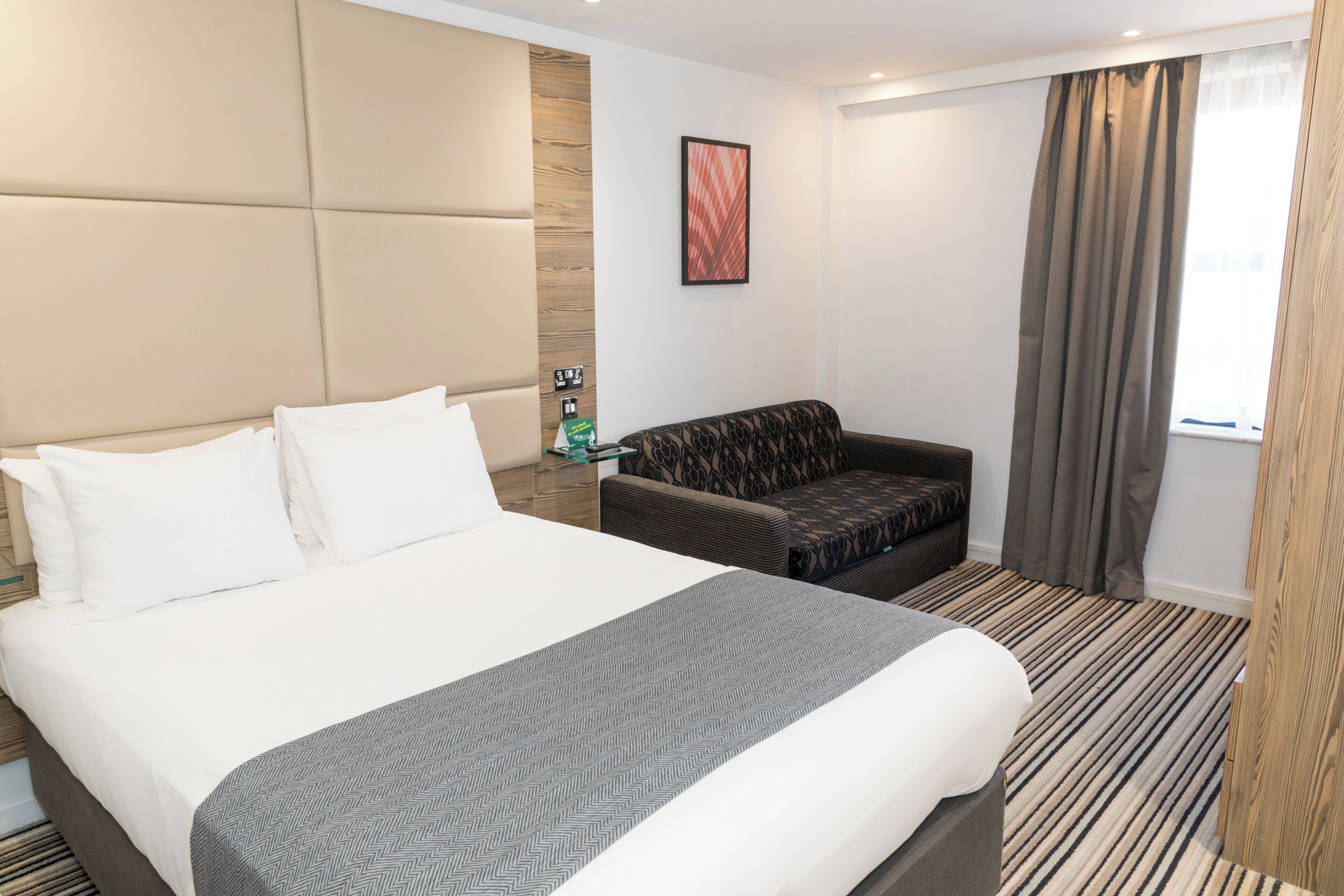 A hotel room with a bed, a sofa, a small table, and a window with curtains.