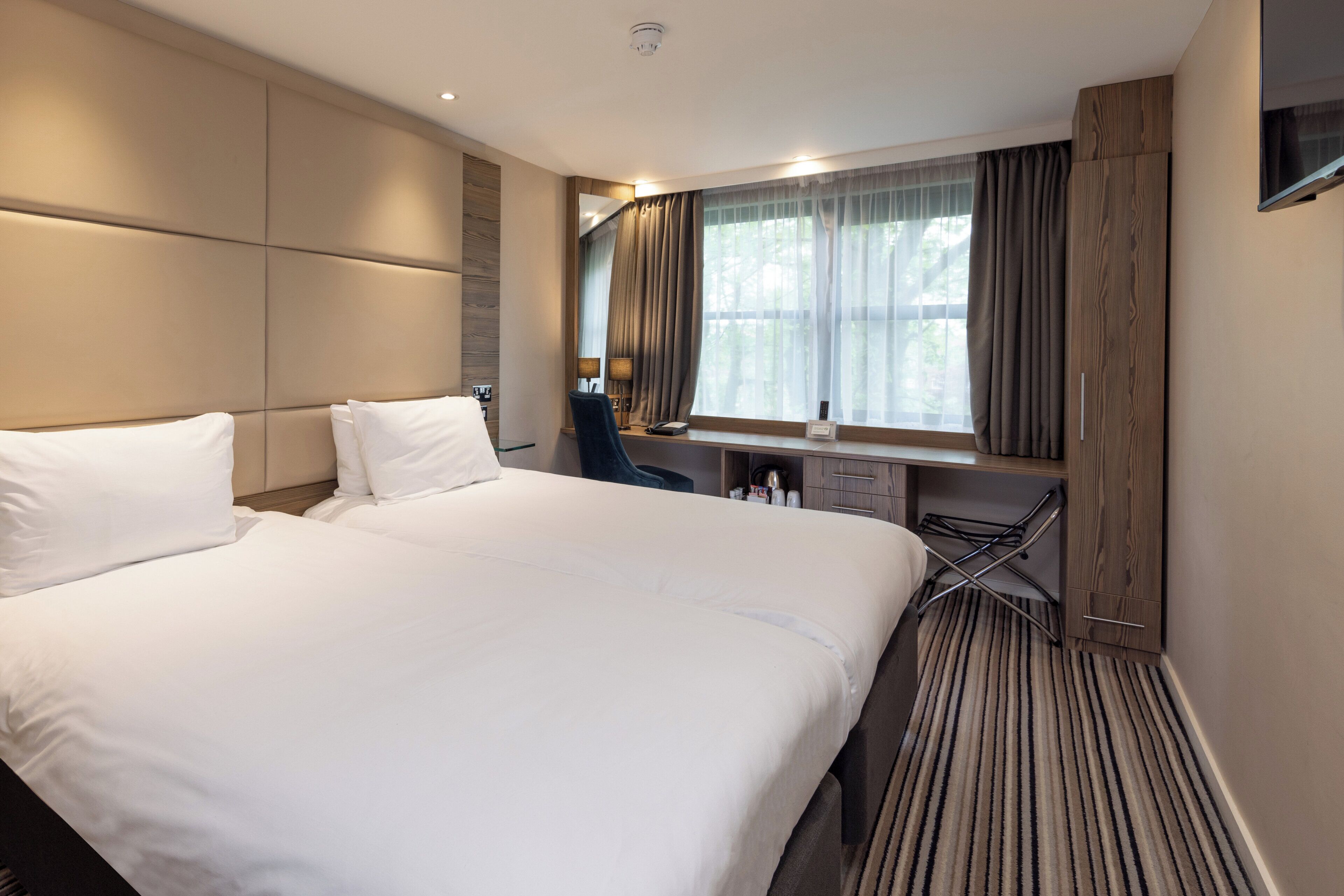 A hotel room with a large bed, a desk, and a window with curtains.