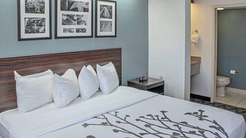 A hotel room with a bed, a nightstand, a clock, and a framed photo collage on the wall.