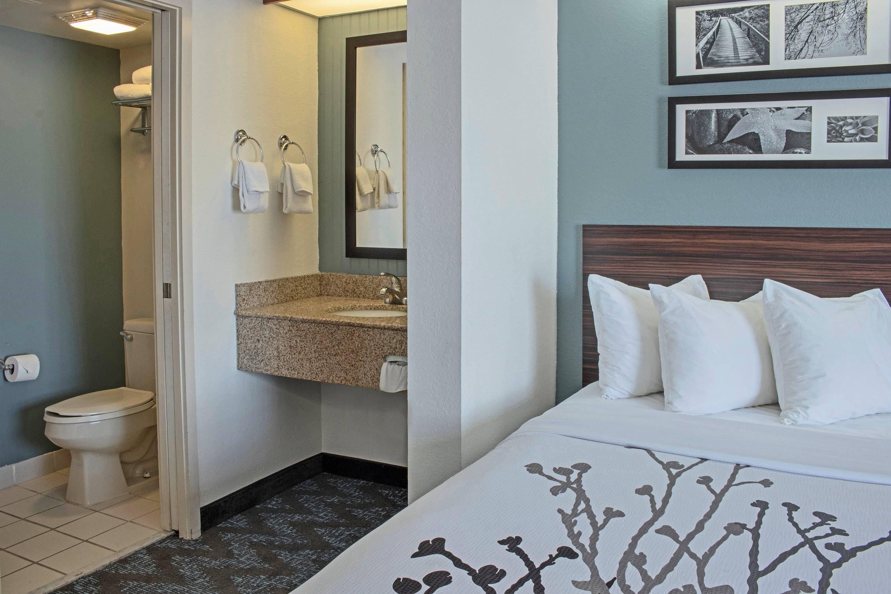 Habitación de hotel con cama, baño con inodoro, lavamanos y toallas.