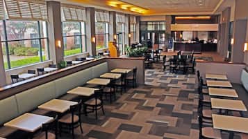 A spacious restaurant with long tables and booths, large windows with views of greenery, and a central counter area.