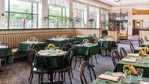 A dining area with tables set for six, each with green tablecloths and sunflowers. Large windows provide natural light and views of trees. - Sleep Inn Lake Wright - Norfolk Airport (Norfolk)