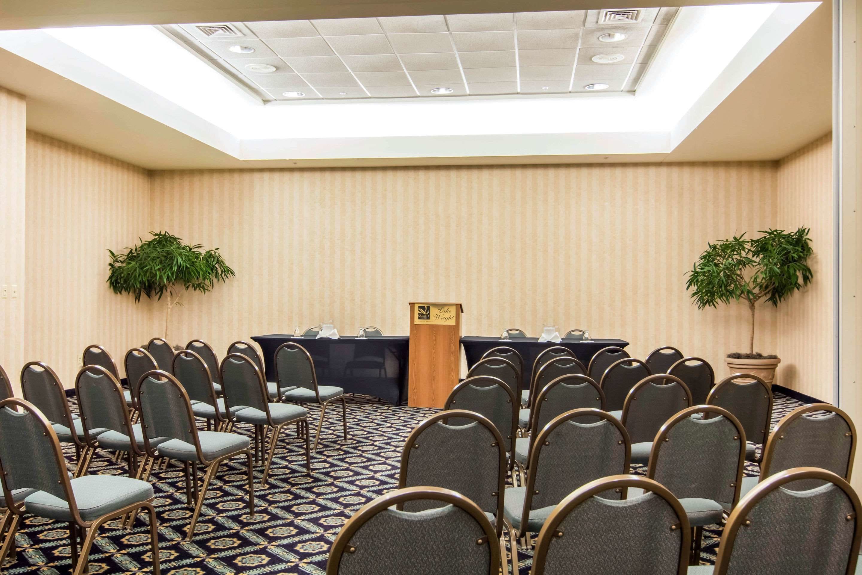 A conference room with rows of chairs, a podium, and two potted plants.