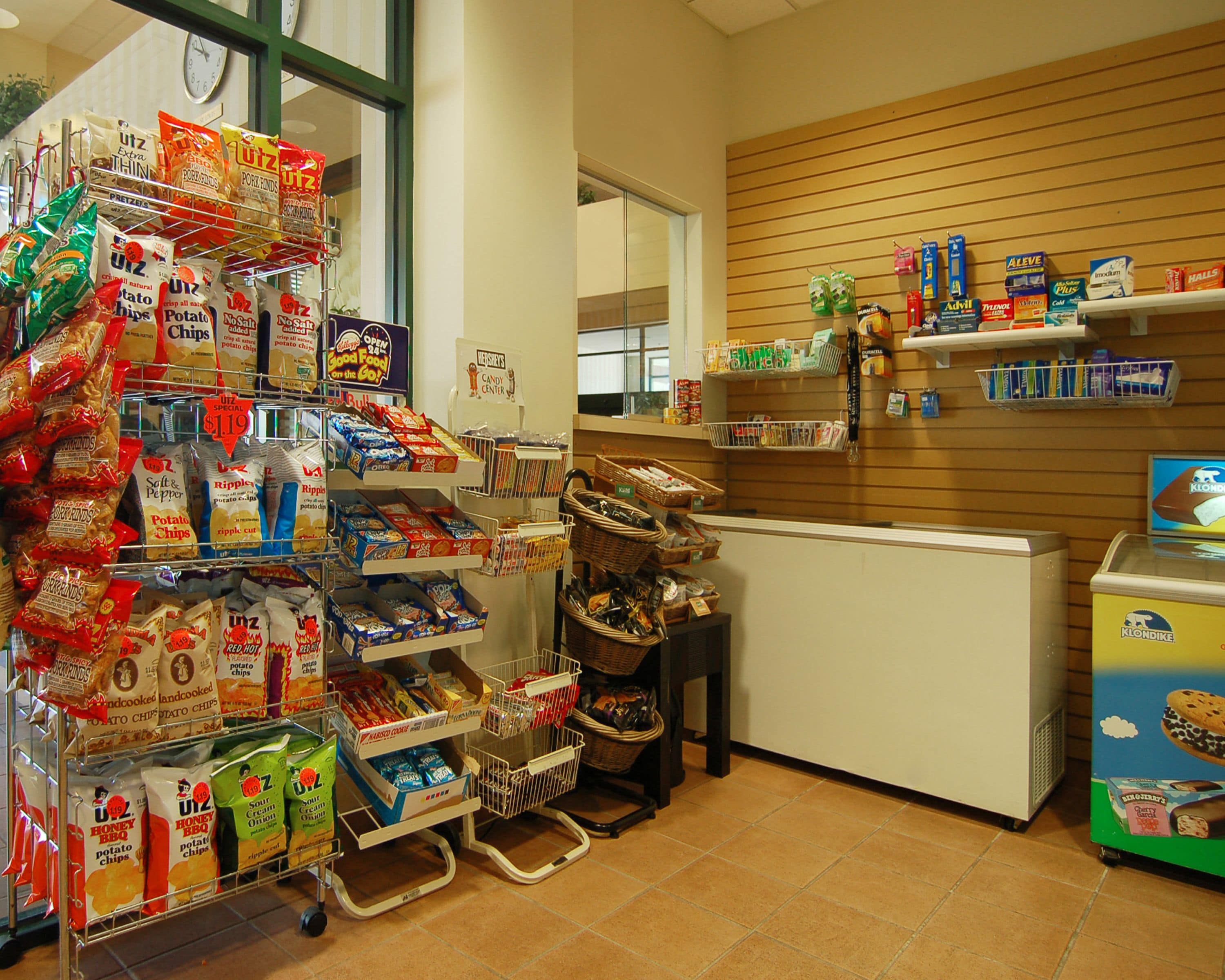 A grocery store interior with shelves stocked with snacks, a refrigerated display, and a checkout counter.