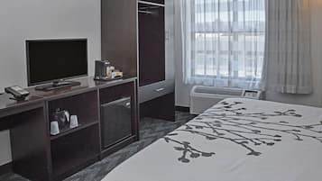 A hotel room with a bed, a TV, a mini-fridge, a coffee machine, a wardrobe, and a window with curtains.