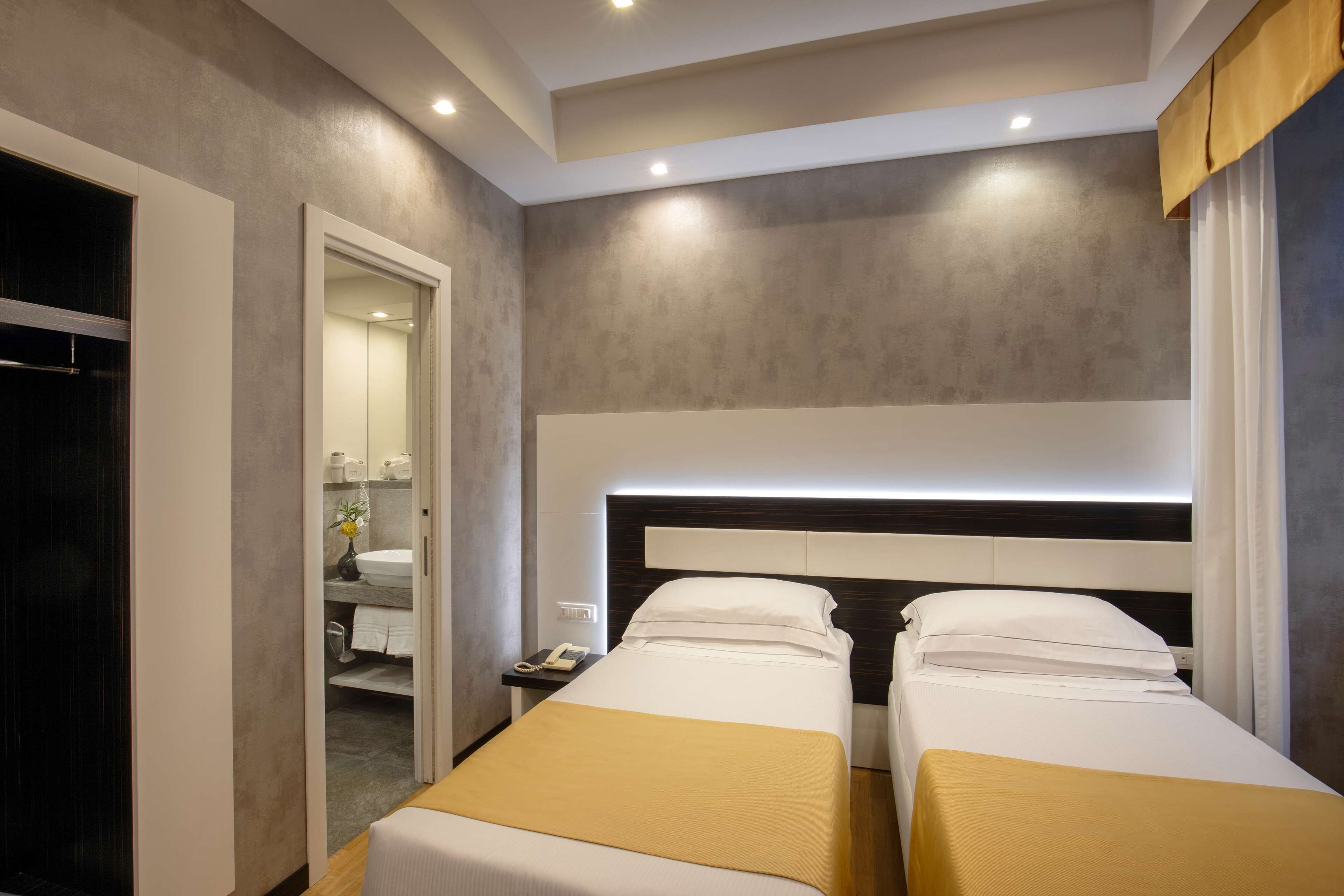 A hotel room with two beds, a bedside table with a phone, and a bathroom visible through an open door.