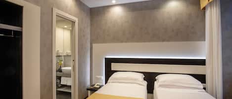 Habitación de hotel con dos camas, una mesita de noche con teléfono y un baño visible a través de una puerta abierta.