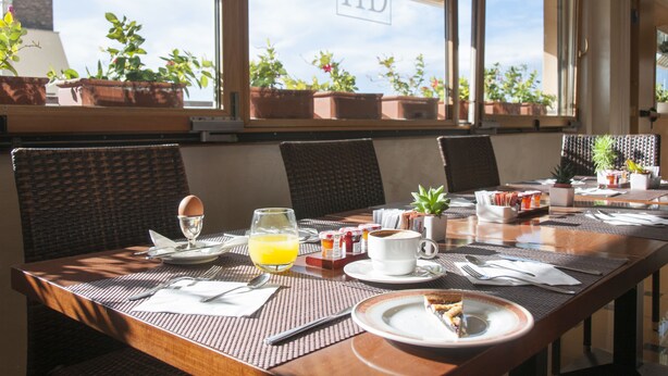 Una mesa de desayuno servida con platos, cubiertos, un vaso de zumo de naranja y una taza de café.
