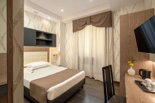 Una camera d'albergo con un letto, una scrivania con sedia, una televisione e una finestra con tende.