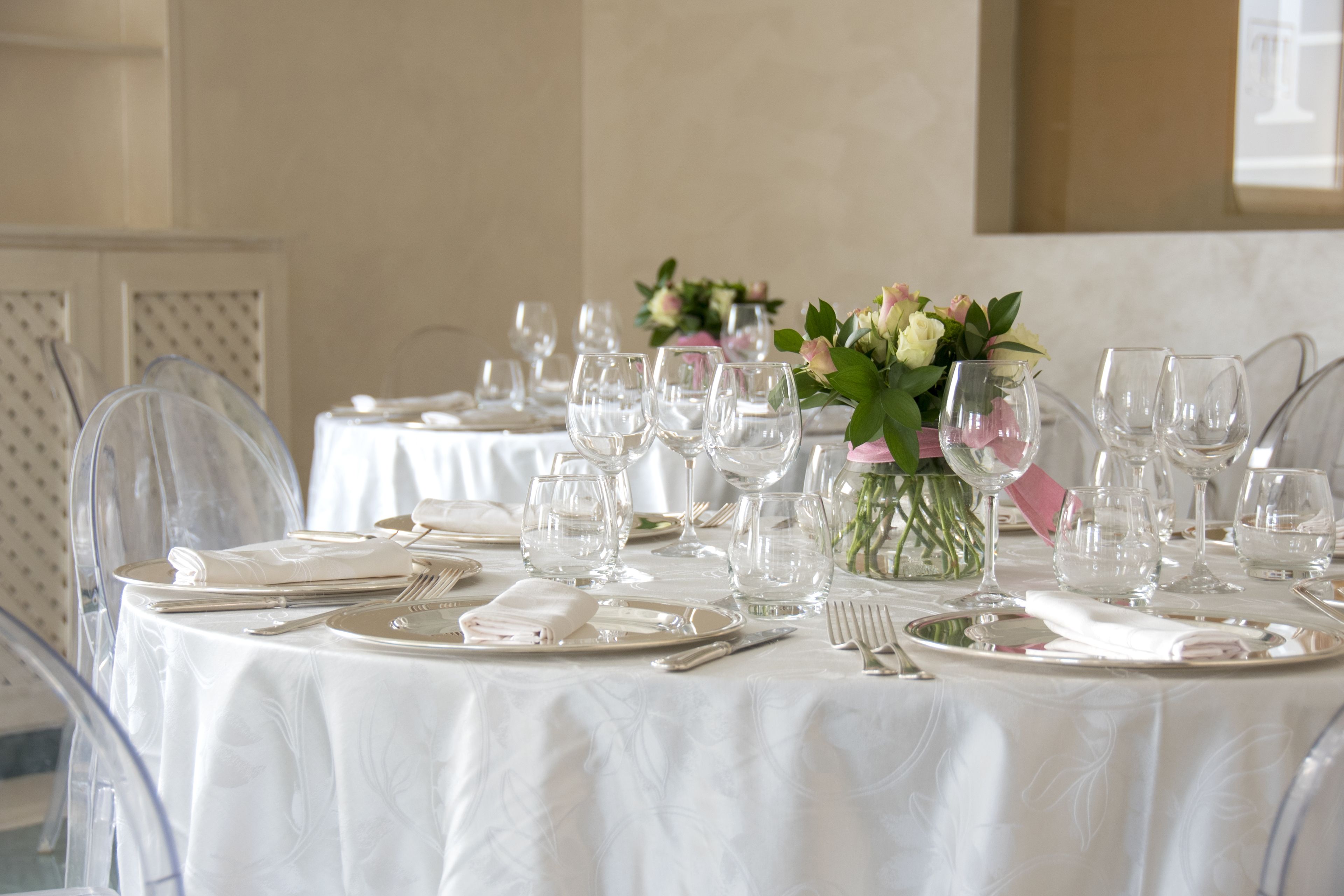 Una mesa dispuesta para un evento formal, con cristalería transparente, servilletas dobladas y un florero con flores.